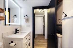 Bathroom with a textured ceiling, stacked washer and dryer, toilet, LVP flooring, and vanity