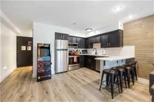 Kitchen featuring kitchen peninsula, a kitchen bar, backsplash, stainless steel appliances, and light LVP flooring