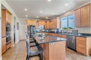 Kitchen with a center island, appliances with stainless steel finishes, a breakfast bar area, and light tile flooring