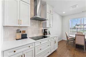 Kitchen featuring backsplash, hardwood / wood-style floors, wall chimney exhaust hood, and black electric cooktop