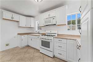 Kitchen featuring sink, white cabinets, white appliances, and light tile floors