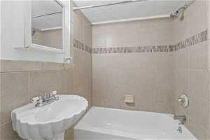 Bathroom with tile walls, a textured ceiling, sink, and tiled shower / bath combo