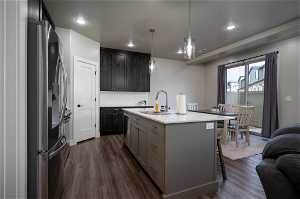 Kitchen with decorative light fixtures, dark hardwood / wood-style flooring, appliances with stainless steel finishes, sink, and an island with sink