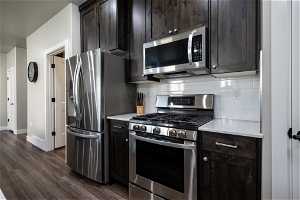 Kitchen with dark brown cabinets, dark hardwood / wood-style flooring, appliances with stainless steel finishes, and backsplash