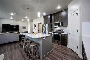 Kitchen featuring appliances with stainless steel finishes, a kitchen bar, sink, dark hardwood / wood-style floors, and a center island with sink