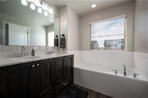 Master bathroom with a healthy amount of sunlight, a bathing tub, hardwood / wood-style floors, and dual vanity