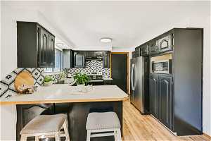 Kitchen with light hardwood / wood-style flooring, kitchen peninsula, stainless steel appliances, sink, and tasteful backsplash