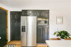 Kitchen featuring appliances with stainless steel finishes, light wood-type flooring, black cabinets