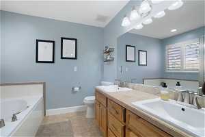 Bathroom with vanity with extensive cabinet space, toilet, double sink, a tub, and tile floors