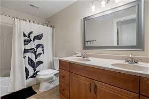 Full bathroom featuring tile floors, shower / bath combo, toilet, and double vanity