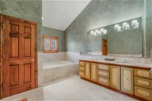 Bathroom featuring dual sinks, oversized vanity, vaulted ceiling, and tiled tub