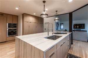 Kitchen with decorative light fixtures, double oven, a center island with sink, light hardwood / wood-style floors, and sink