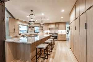 Kitchen featuring light stone countertops, appliances with stainless steel finishes, an island with sink, pendant lighting, and light wood-type flooring