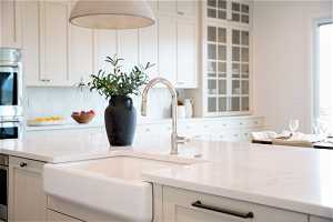 Kitchen featuring sink, backsplash, white cabinetry, and light stone counters