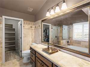 Bathroom featuring vanity with extensive cabinet space, lofted ceiling, toilet, tile floors, and a bathtub
