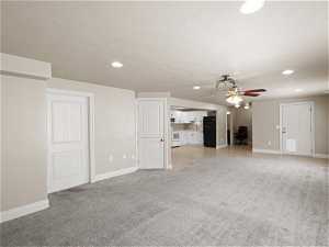 Unfurnished living room featuring light colored carpet, ceiling fan, and a textured ceiling