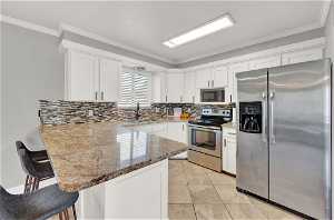 Kitchen featuring white cabinets, appliances with stainless steel finishes, backsplash, and a kitchen breakfast bar