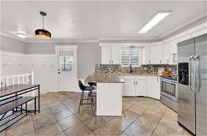 Kitchen featuring ornamental molding, pendant lighting, stainless steel appliances, and a breakfast bar area