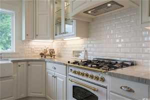 Kitchen with white cabinets, tasteful backsplash, high end range, and light stone counters