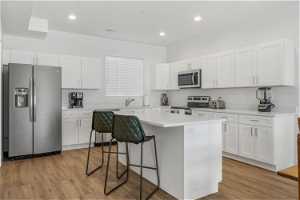 Kitchen featuring appliances with stainless steel finishes, a center island, white cabinets, light hardwood / wood-style floors, and a breakfast bar area