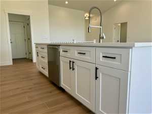 Kitchen with vaulted ceiling, light hardwood / wood-style floors, white cabinets, and stainless steel dishwasher