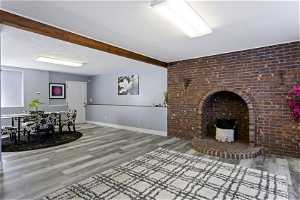 Living room with a fireplace, brick wall, beam ceiling, hardwood / wood-style flooring, and a textured ceiling