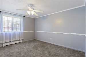 Carpeted empty room featuring ceiling fan, crown molding, and baseboard heating