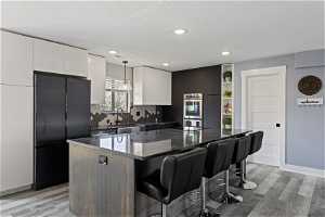 Kitchen with a center island, backsplash, white cabinetry, decorative light fixtures, and black refrigerator