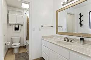 Full bathroom featuring shower / bathtub combination, toilet, tile flooring, vanity, and a skylight