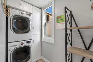 Clothes washing area featuring cabinets and stacked washing maching and dryer