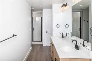 Bathroom with large vanity, a shower with shower door, a textured ceiling, hardwood / wood-style floors, and dual sinks