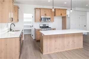 Kitchen featuring a center island, light brown cabinetry, light hardwood / wood-style floors, decorative light fixtures, and stainless steel appliances