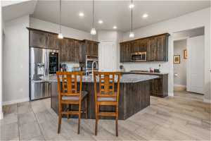 Kitchen with backsplash, stainless steel appliances, an island with sink, dark brown cabinetry, and pendant lighting
