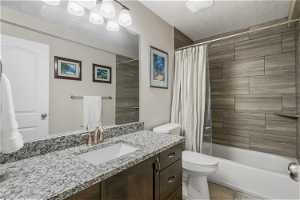 Full bathroom featuring tile flooring, vanity with extensive cabinet space, a textured ceiling, shower / bath combination with curtain, and toilet
