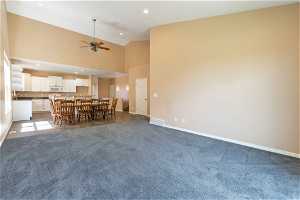 Unfurnished living room featuring carpet flooring, ceiling fan, high vaulted ceiling.