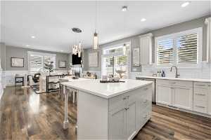Kitchen with white cabinets, sink, backsplash, hanging light fixtures, and dark hardwood / wood-style floors