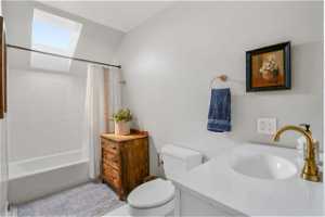 Full bathroom with shower / bath combo with shower curtain, toilet, lofted ceiling with skylight, and vanity