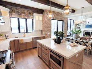 Kitchen with a kitchen island, appliances with stainless steel finishes, light hardwood / wood-style flooring, decorative light fixtures, and brick wall