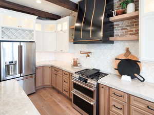 Kitchen featuring white cabinets, light stone countertops, light hardwood / wood-style flooring, beamed ceiling, and high end appliances