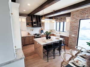 Kitchen featuring a kitchen island, range hood, white cabinets, appliances with stainless steel finishes, and light hardwood / wood-style floors