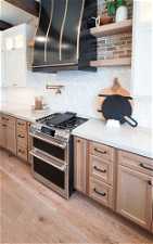 Kitchen featuring light stone counters, double oven range, white cabinets, light hardwood / wood-style floors, and backsplash