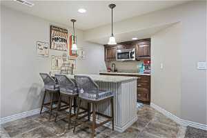 Kitchen with light stone countertops, kitchen peninsula, hanging light fixtures, dark tile flooring, and a breakfast bar
