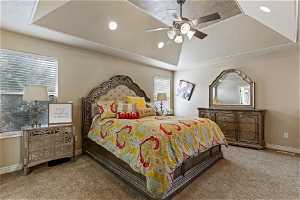 Carpeted bedroom with ceiling fan, a raised ceiling, and multiple windows