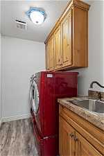 Laundry room with cabinets, a textured ceiling, dark wood-type flooring, washing machine and clothes dryer, and sink