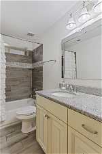 Full bathroom featuring wood-type flooring, large vanity, shower / bath combination with curtain, and toilet