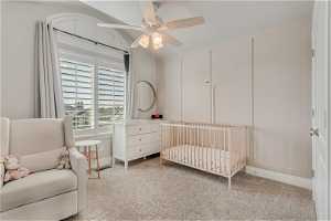 Carpeted bedroom with ceiling fan and a crib