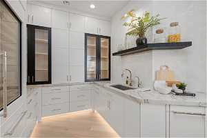 Kitchen with white cabinets, tasteful backsplash, light stone countertops, and light hardwood / wood-style floors