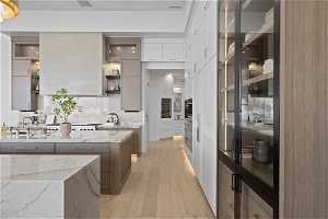 Kitchen with white cabinetry, tasteful backsplash, light stone counters, sink, and light wood-type flooring