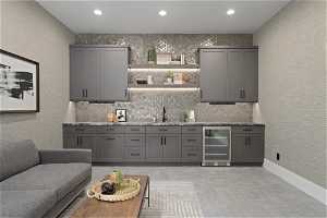 Bar featuring light stone countertops, sink, backsplash, beverage cooler, and gray cabinetry