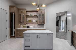 Kitchen with light stone countertops, a kitchen island, hanging light fixtures, tasteful backsplash, and light tile floors